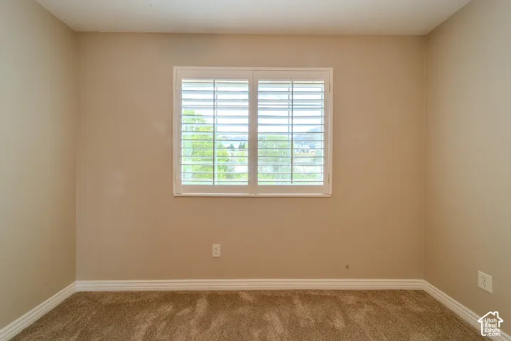 Window with white plantation shutters, neutral wall paint, white baseboards, and brown carpeting