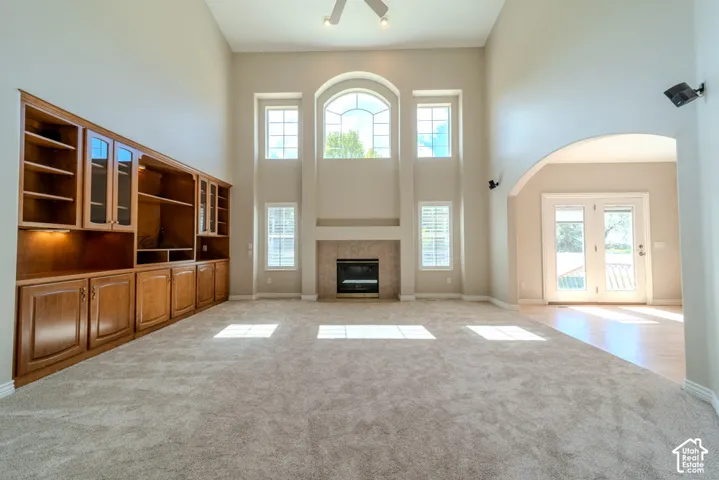 Vaulted ceiling living area featuring a built-in wood entertainment center with glass-front cabinets, a fireplace with a light-colored surround, and multiple tall windows including an arched transom