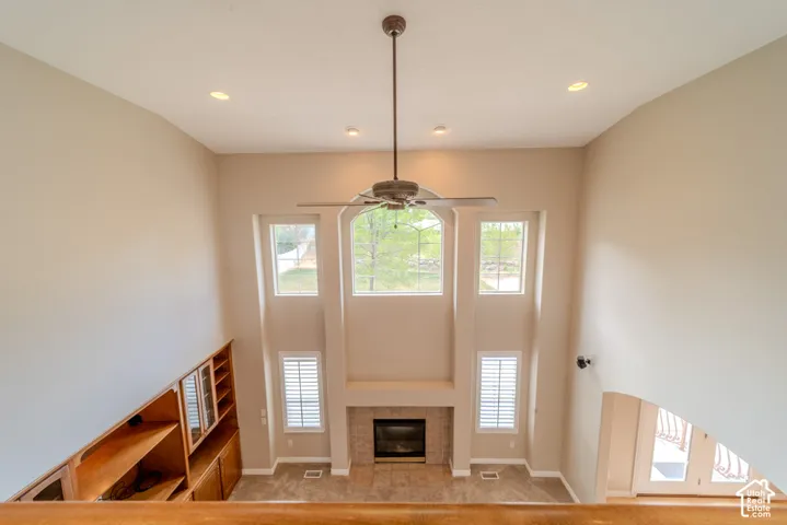 Two-story living area featuring a fireplace with a tile surround, a ceiling fan, recessed lighting, and a built-in shelving unit with glass-front cabinetry