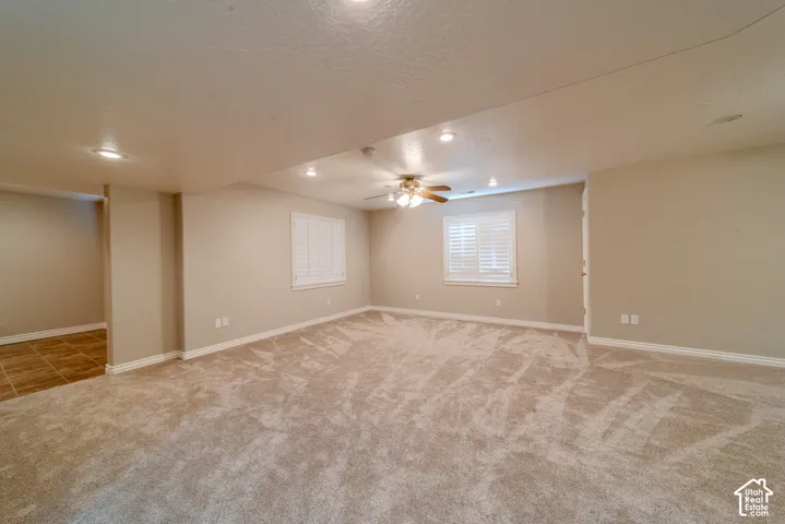 Spacious room featuring plush carpet flooring, recessed lighting, two windows with white plantation shutters, a ceiling fan, and neutral-toned walls