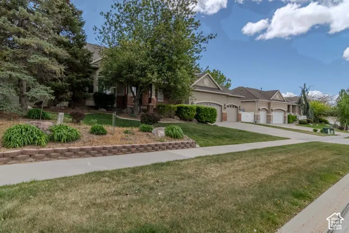Residential streetscape showcasing a stucco and brick exterior, multi-car garage, concrete driveway, and a retaining wall with mature landscaping
