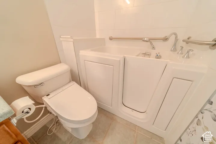 Bathroom featuring a white walk-in tub with grab bars, a handheld shower, and polished chrome fixtures