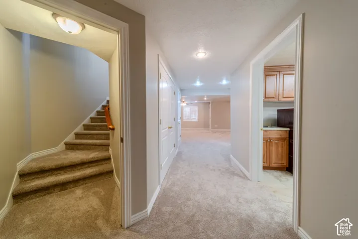 Carpeted staircase with wood handrail, recessed lighting, and a neutral color palette