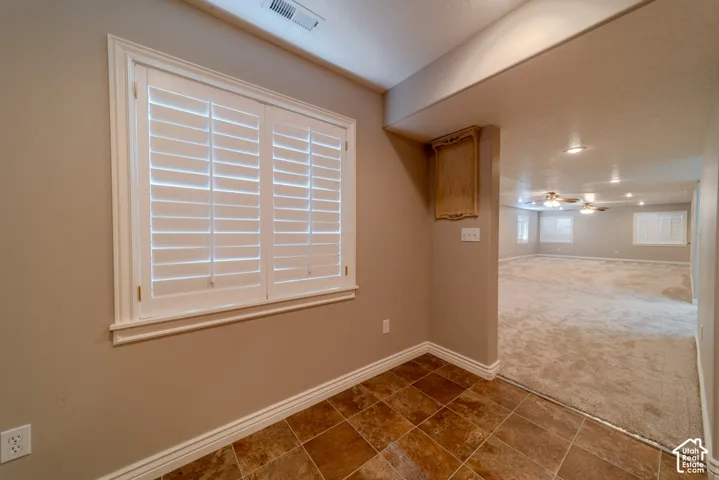 Window with white plantation shutters, tile flooring, baseboard molding, and wall-mounted light fixture