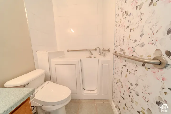 Bathroom featuring a white walk-in tub with grab bars, complemented by a white toilet and a vanity with a light-colored countertop