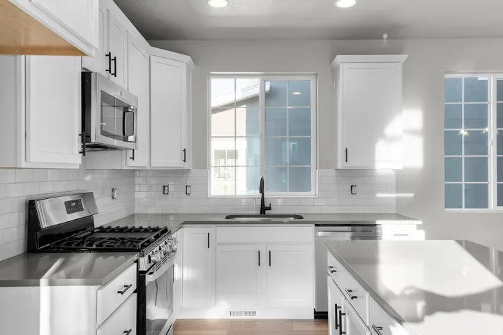 Modern kitchen featuring white shaker cabinetry with matte black hardware, stainless steel appliances, a subway tile backsplash, and light-toned countertops