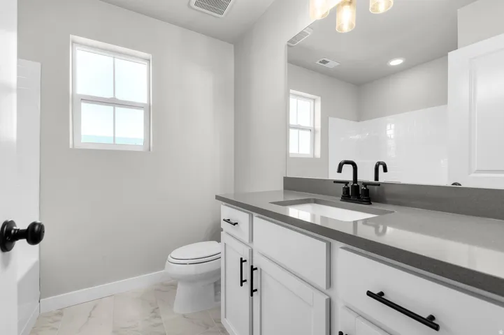 Contemporary bathroom featuring a white vanity with dark hardware, an integrated sink, and a gray countertop