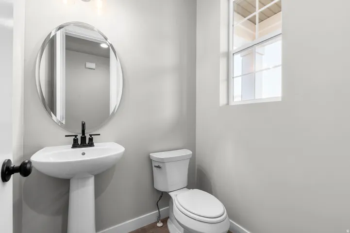 Pedestal sink with matte black hardware, oval mirror, and a toilet
