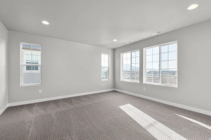 Spacious room featuring multiple grid-pattern windows, recessed lighting, neutral wall paint, white baseboards, and patterned carpet flooring