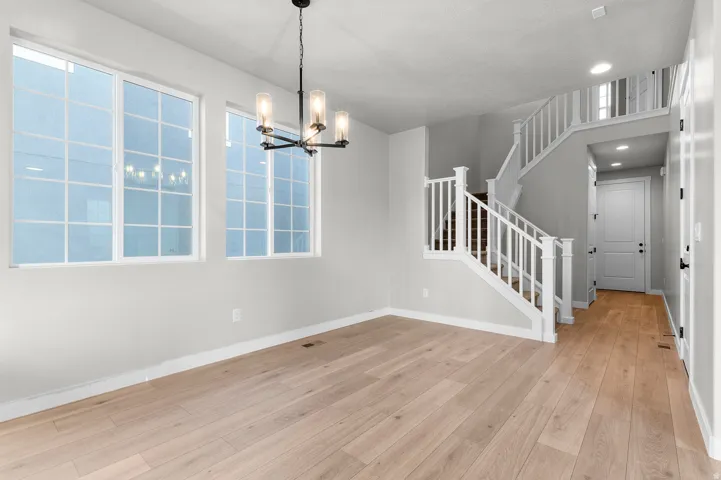 Open concept space with light wood-finish flooring, featuring a contemporary chandelier and abundant natural light from large grid windows