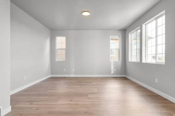 Bright interior space with light wood-finish flooring, light gray walls, white baseboards, and multiple large windows for abundant illumination