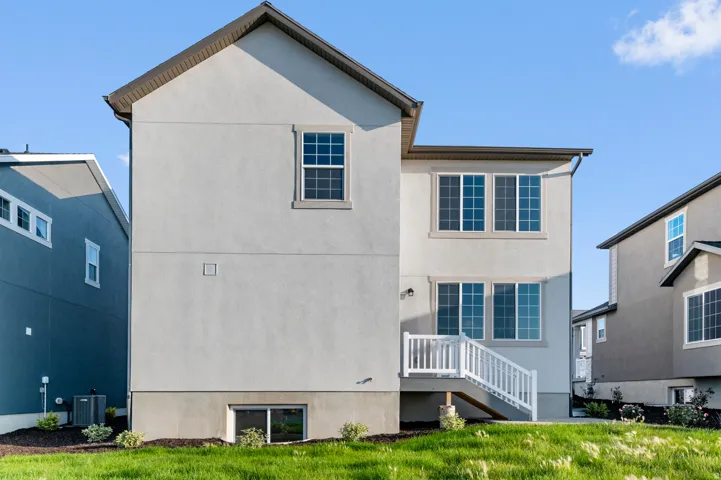 Rear exterior featuring stucco finish, multiple windows, a white deck, white railings, and a manicured lawn