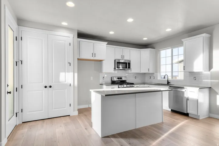 Bright kitchen featuring white cabinetry, a central island, stainless steel appliances, recessed lighting, and wood-finish flooring