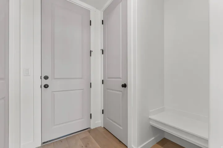 Entryway featuring wood-finish flooring, white panel doors with black hardware, and a built-in bench with a white countertop