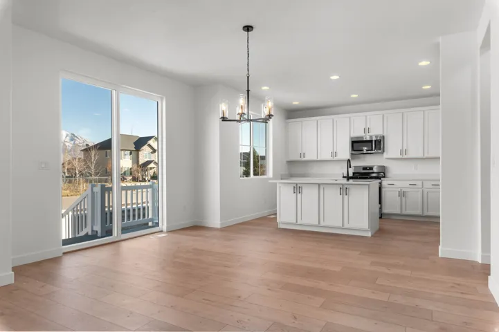 Open-concept living area featuring light wood-finish flooring, white shaker cabinetry, stainless steel appliances, and a central island with an undermount sink