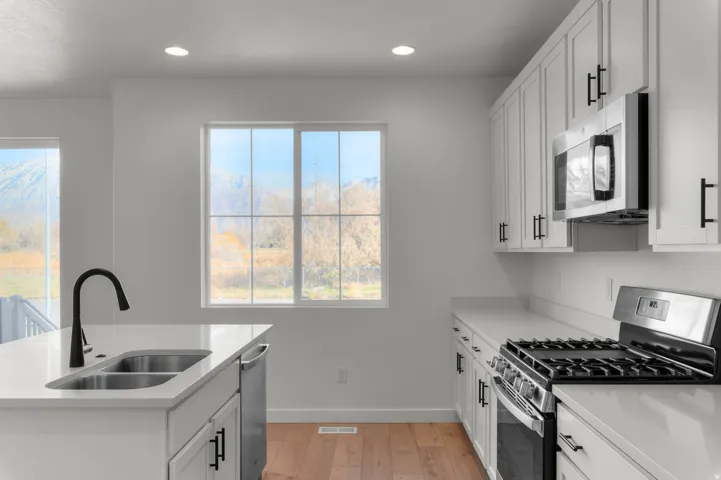 Modern kitchen featuring white shaker cabinetry, stainless steel appliances, light countertops, a kitchen island with a double sink and gooseneck faucet, and wood-finish flooring