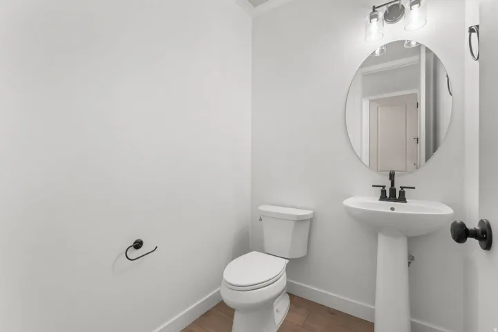 Pedestal sink with matte black faucet, round mirror, and a two-bulb vanity light fixture