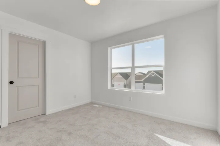 Light-filled interior space featuring neutral carpeting, white walls, and a two-panel door with black hardware
