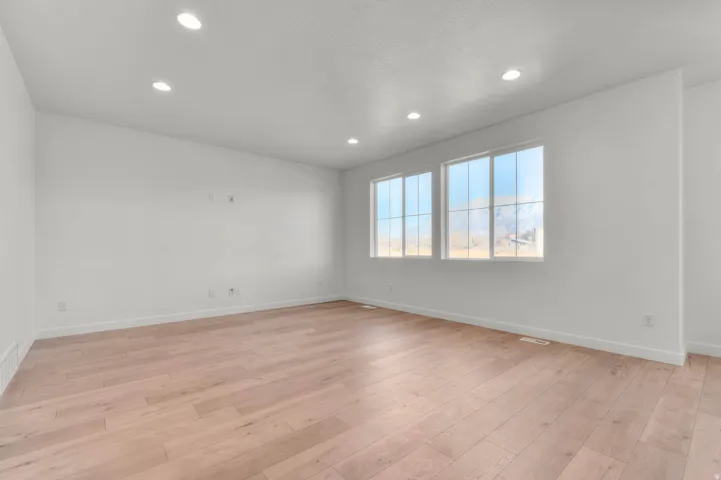 Spacious room featuring light wood-finish flooring, recessed lighting, and two large windows with grid patterns