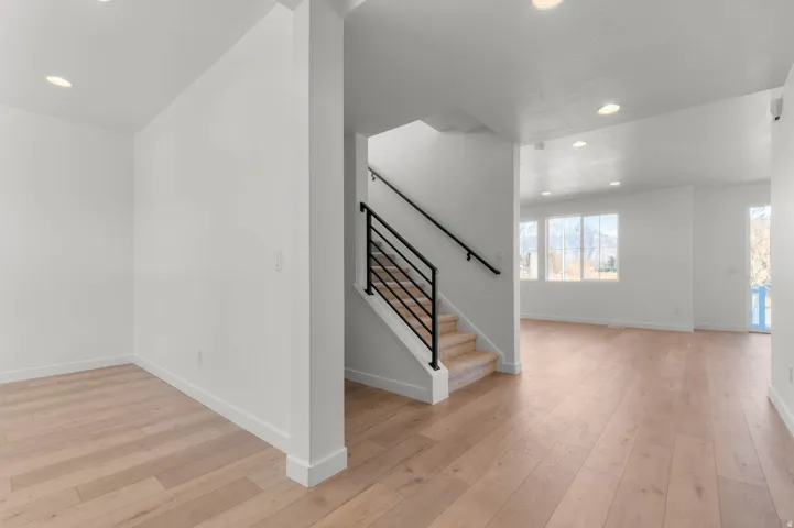 Open-concept interior featuring wood-finish flooring, recessed lighting, a modern staircase with black railing, and abundant natural light from multiple windows