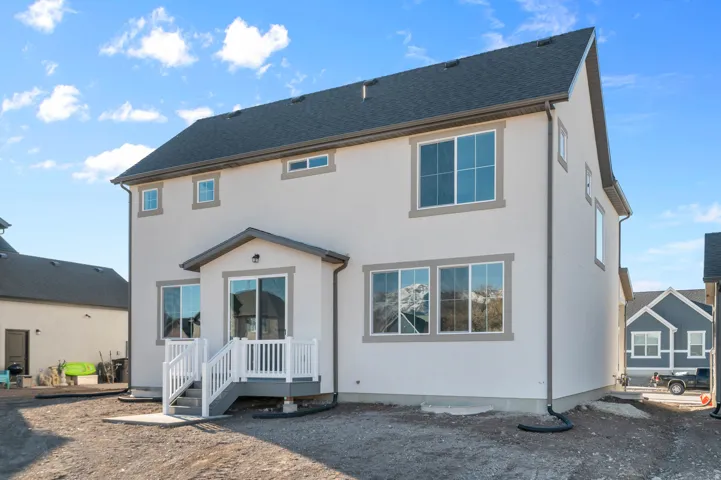 Rear exterior featuring stucco siding with contrasting trim, a dark shingled roof, multiple windows, and a raised deck with white railings