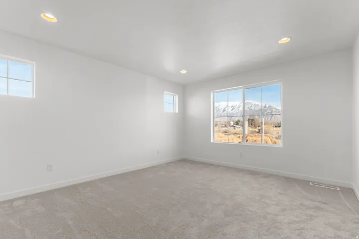 Spacious room featuring light gray carpeting, recessed ceiling lighting, and multiple windows