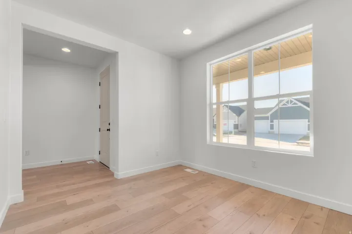 Bright interior space featuring a large multi-pane window, light wood-finish flooring, recessed lighting, and a white interior door with black hardware