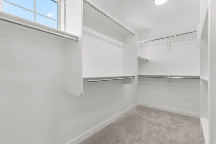Walk-in closet featuring white built-in shelving, multiple hanging rods, and a window with grid panes