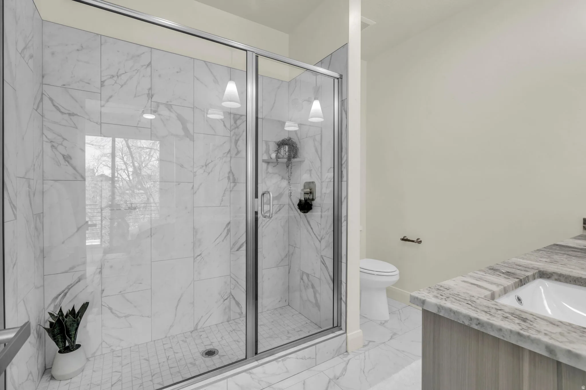 Glass-enclosed shower with white marble-look tile, dual pendant lights, and a built-in shower niche