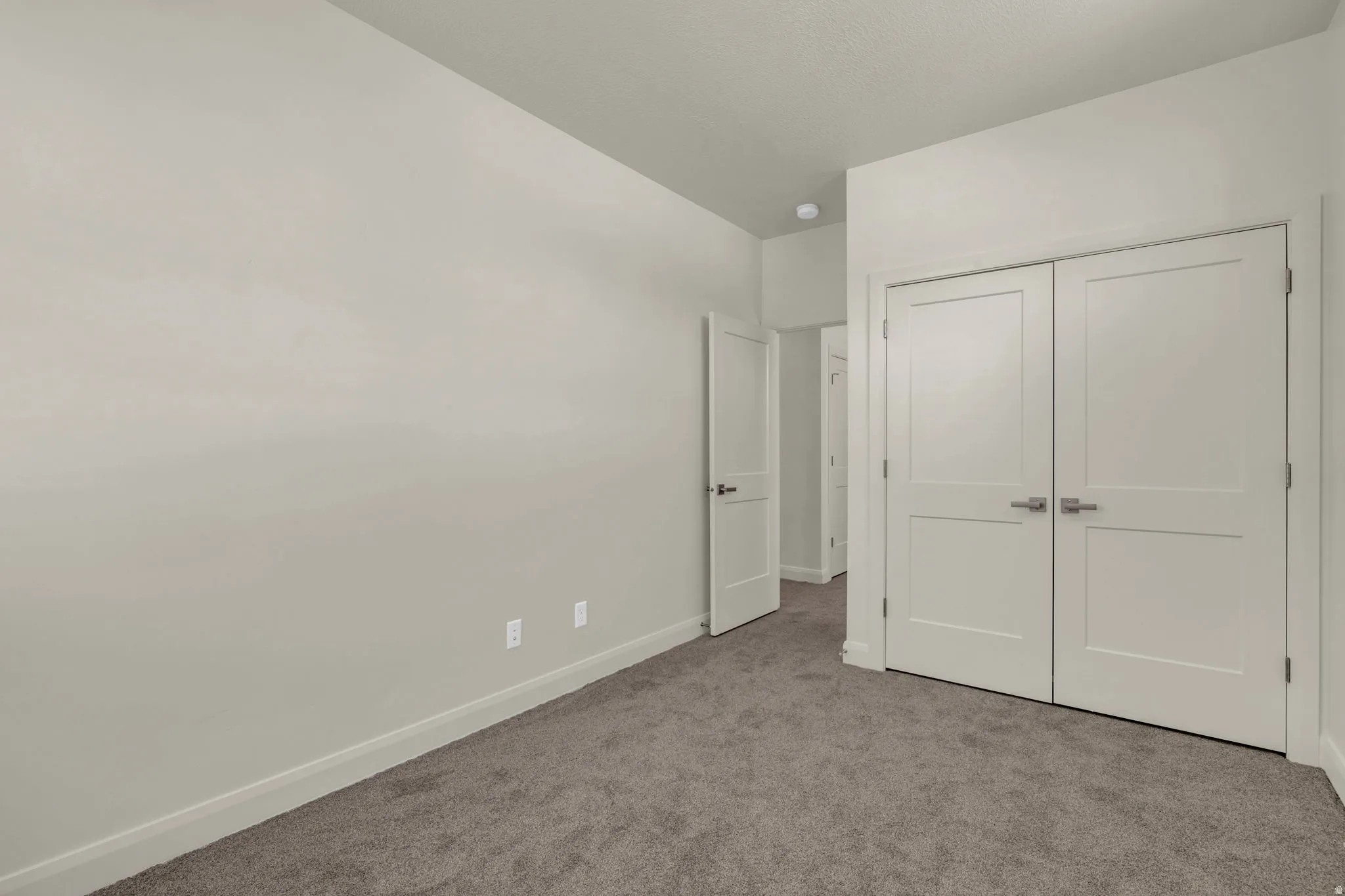 Neutral-toned interior room featuring light gray walls, dark gray carpeting, and white baseboards