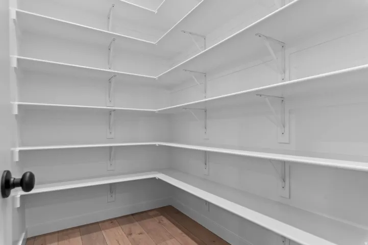 Corner pantry featuring extensive white shelving, wood-finish flooring, and a contemporary black door handle