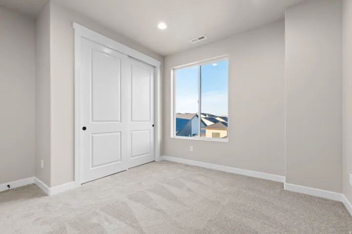 Neutral-toned room featuring a large window, light-colored carpet, white trim, and a bi-fold closet with panel doors and matte black hardware