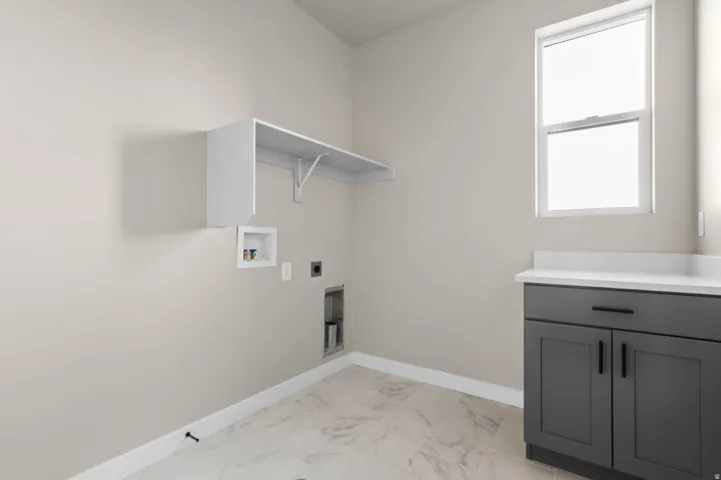 Utility room featuring a single window, built-in shelving, white baseboards, a dark gray storage cabinet with a white countertop, and light-toned tile flooring