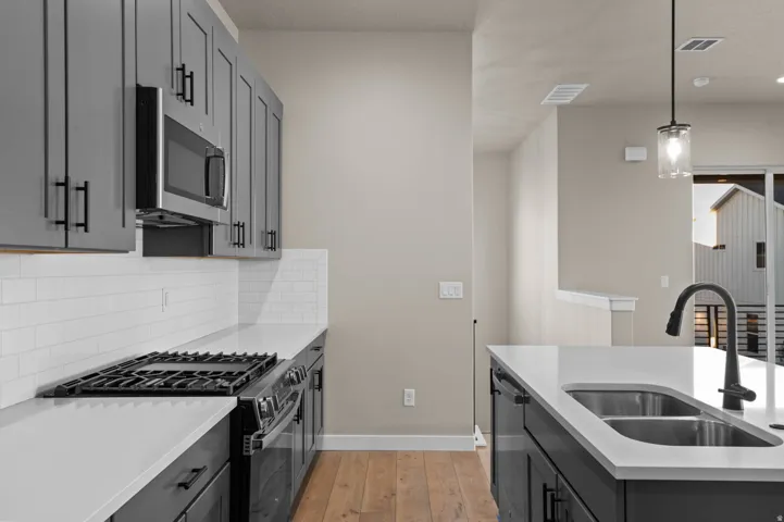 Contemporary kitchen featuring gray shaker-style cabinetry, stainless steel appliances, white subway tile backsplash, and light-toned countertops