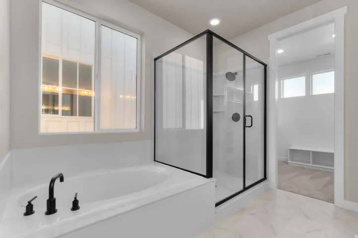 Bathroom featuring a built-in soaking tub with matte black fixtures, a separate glass-enclosed shower with black trim, and large format floor tile