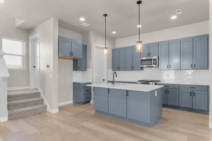 Kitchen featuring a central island, blue cabinetry, stainless steel appliances, quartz countertops, white subway tile backsplash, and light wood-finish flooring