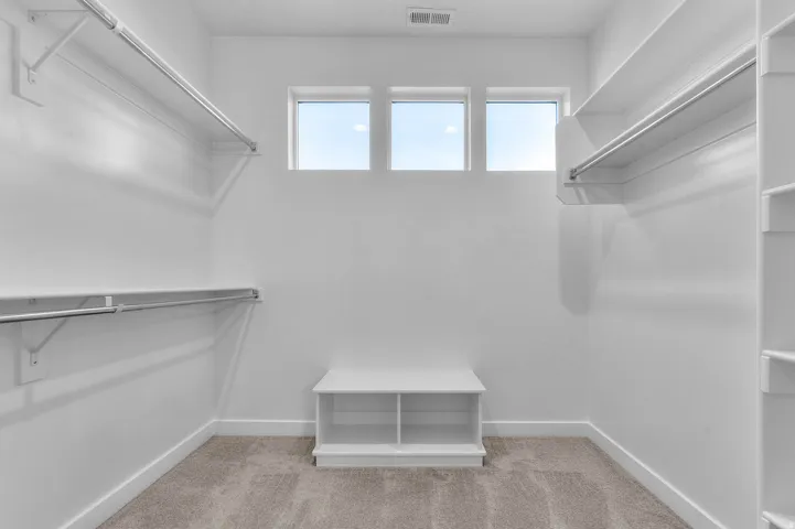 Spacious closet featuring multiple hanging rods, built-in shelving, a built-in bench, and three transom windows