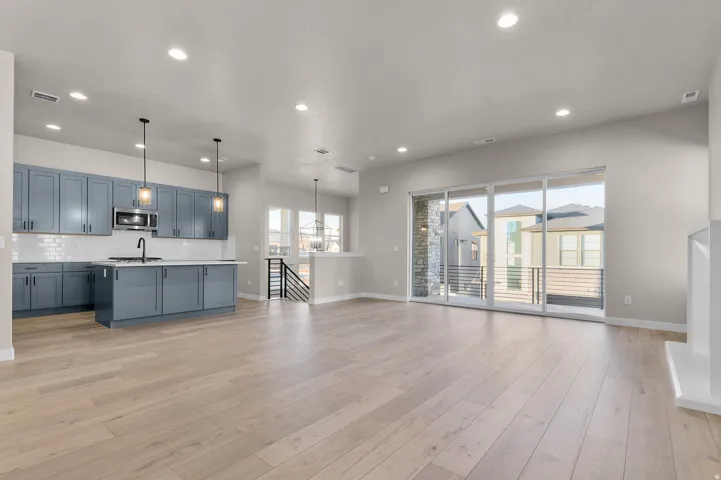 Open-concept living area featuring light wood-finish flooring, recessed lighting, and a modern kitchen with blue cabinetry