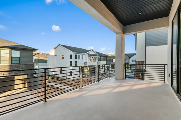 Spacious covered balcony featuring a light-colored concrete surface, modern black horizontal railings, and an overhead ceiling with recessed lighting