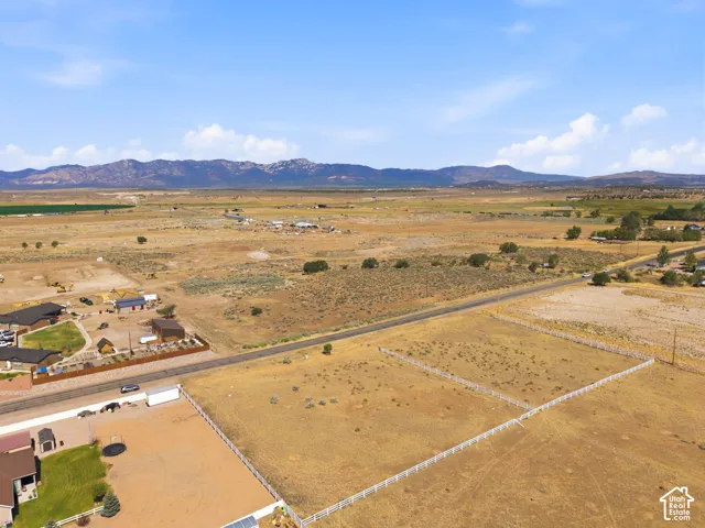 Expansive vacant land parcels featuring white fencing, a paved road, and distant mountain backdrops