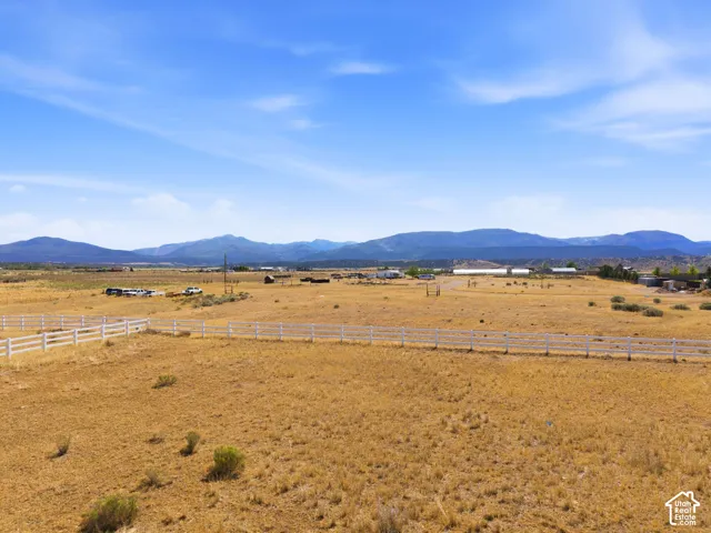 Expansive open field with white multi-rail fencing and distant mountain ranges