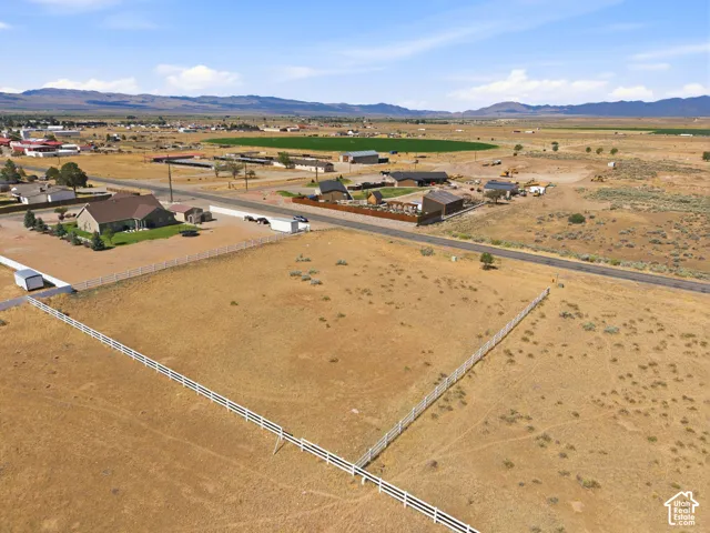 Expansive undeveloped land parcel featuring a white three-rail fence, a paved road border, and distant mountain scenery