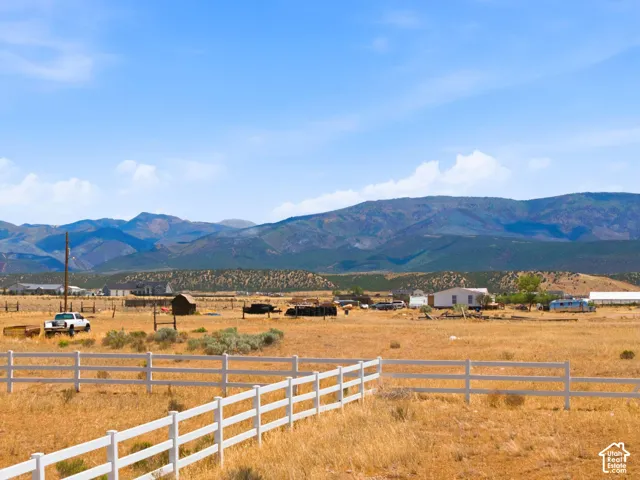 Expansive rural landscape featuring a white fence, dry grasses, and distant mountains under a blue sky
