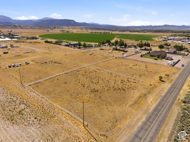 Expansive undeveloped land featuring a paved road frontage, perimeter fencing, and distant mountain backdrops