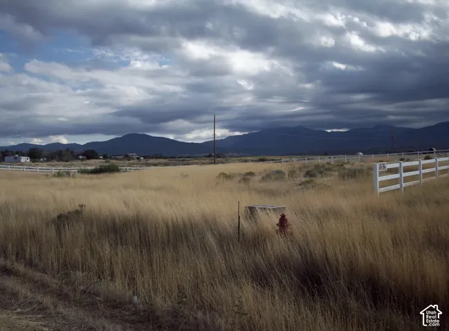 Expansive natural landscape featuring golden dry grasses, a white three-rail fence, and distant mountains under a cloudy sky