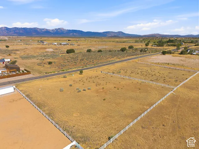 Expansive land parcel featuring white perimeter fencing, a paved road frontage, and distant mountain scenery