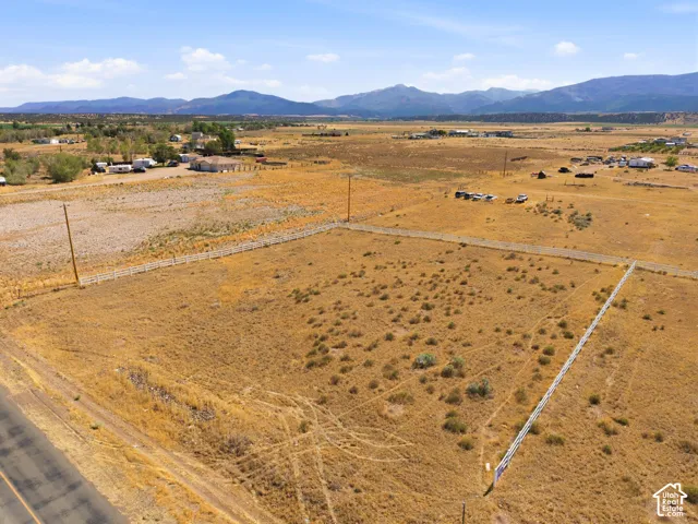 Expansive land parcel with partial white fencing, a roadside location, and distant mountain backdrops