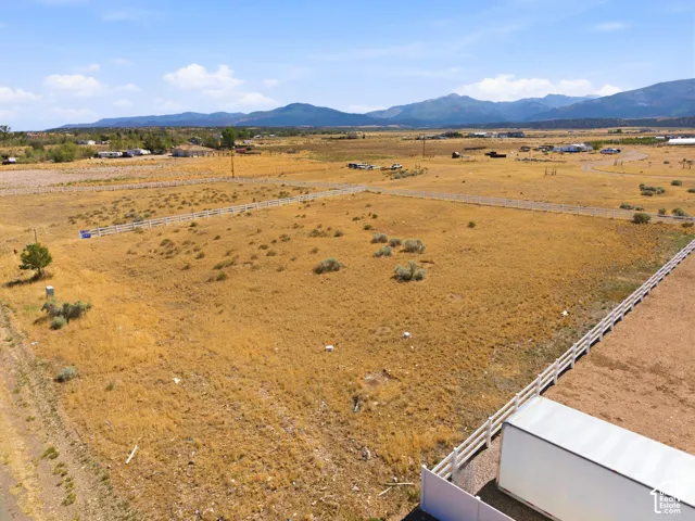 Expansive open land with a white perimeter fence, featuring a dry, grassy landscape and scattered low-lying shrubs
