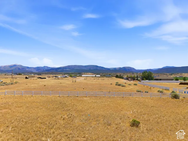 Expansive natural landscape featuring a white perimeter fence, distant mountain ranges, and clear skies
