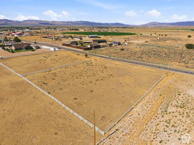 Expansive, level land parcel featuring perimeter fencing, a paved road frontage, and a distant mountain backdrop